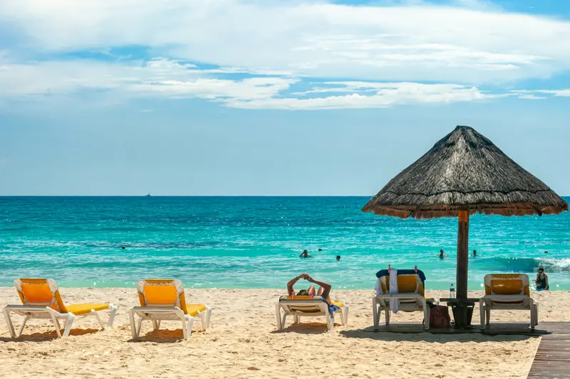 Sun loungers and a palm-thatched parasol on a white beach in Cancún