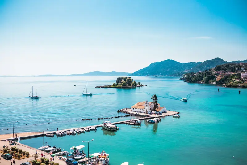 A small monastery islet and boats in clear water in Corfu