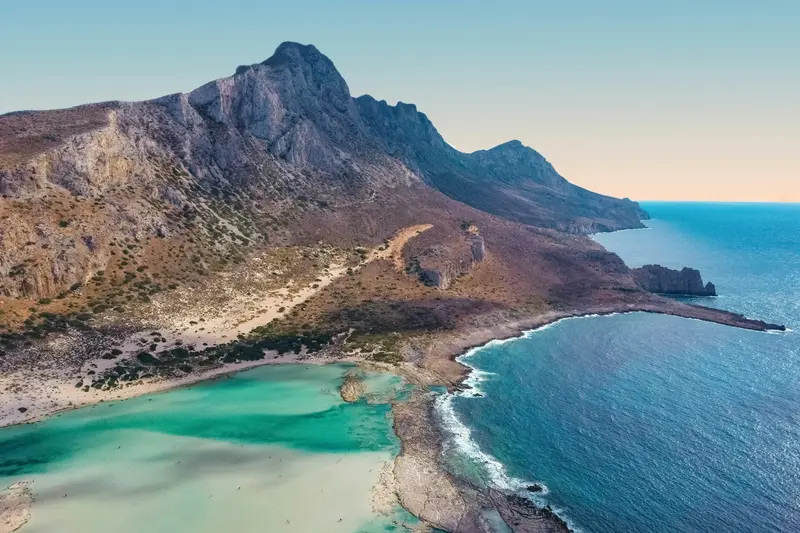 A shallow turquoise lagoon below mountains in Crete