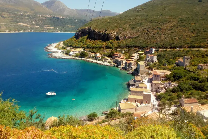 A turquoise bay and small village below green hills on a Greek coast