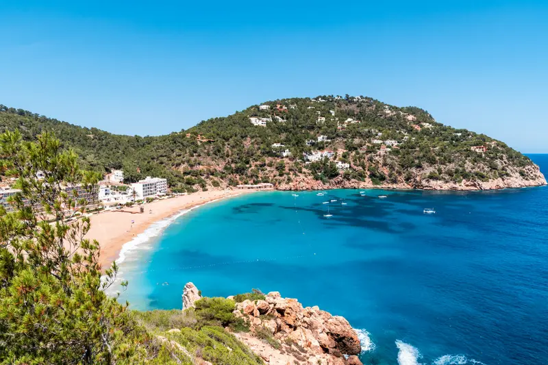 A sandy cove with clear blue water and green hills in Ibiza