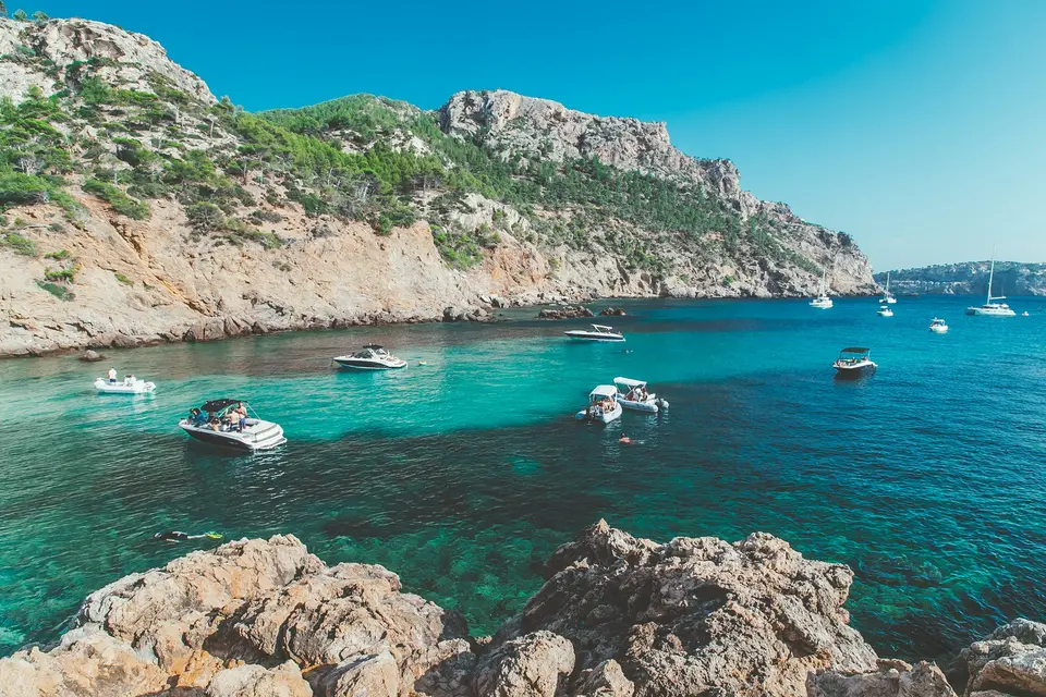 Boats in a turquoise bay below green hills in Majorca